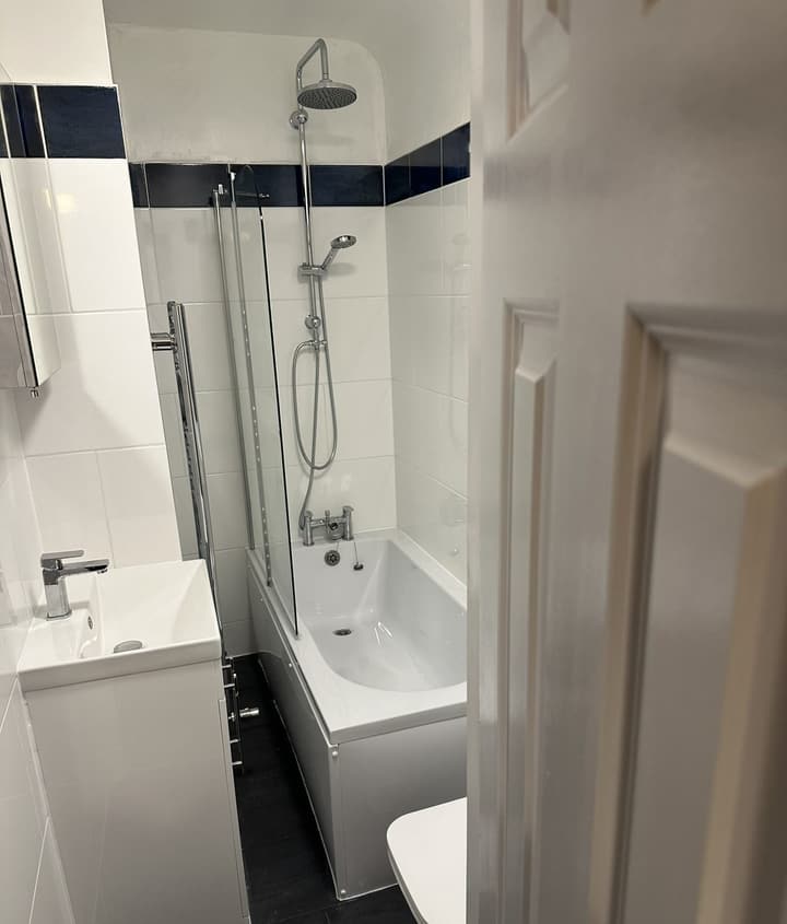 Finished Barnet bathroom: white bath with glass screen, chrome thermostatic shower riser, vanity basin and dark floor tiles