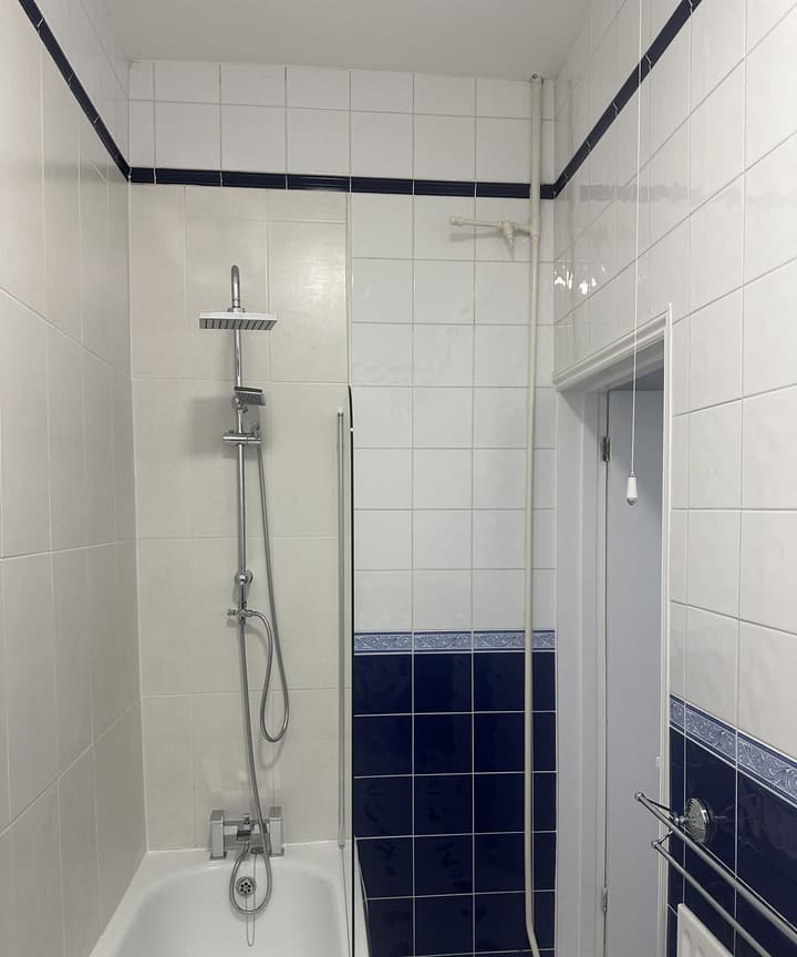 Camden Town bathroom after a partial renovation: new chrome rainfall shower riser and bath mixer over a white bath