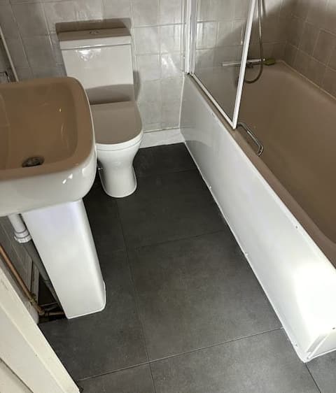 Islington bathroom after: new grey floor tiles and a clean white bath panel with the toilet and basin refitted